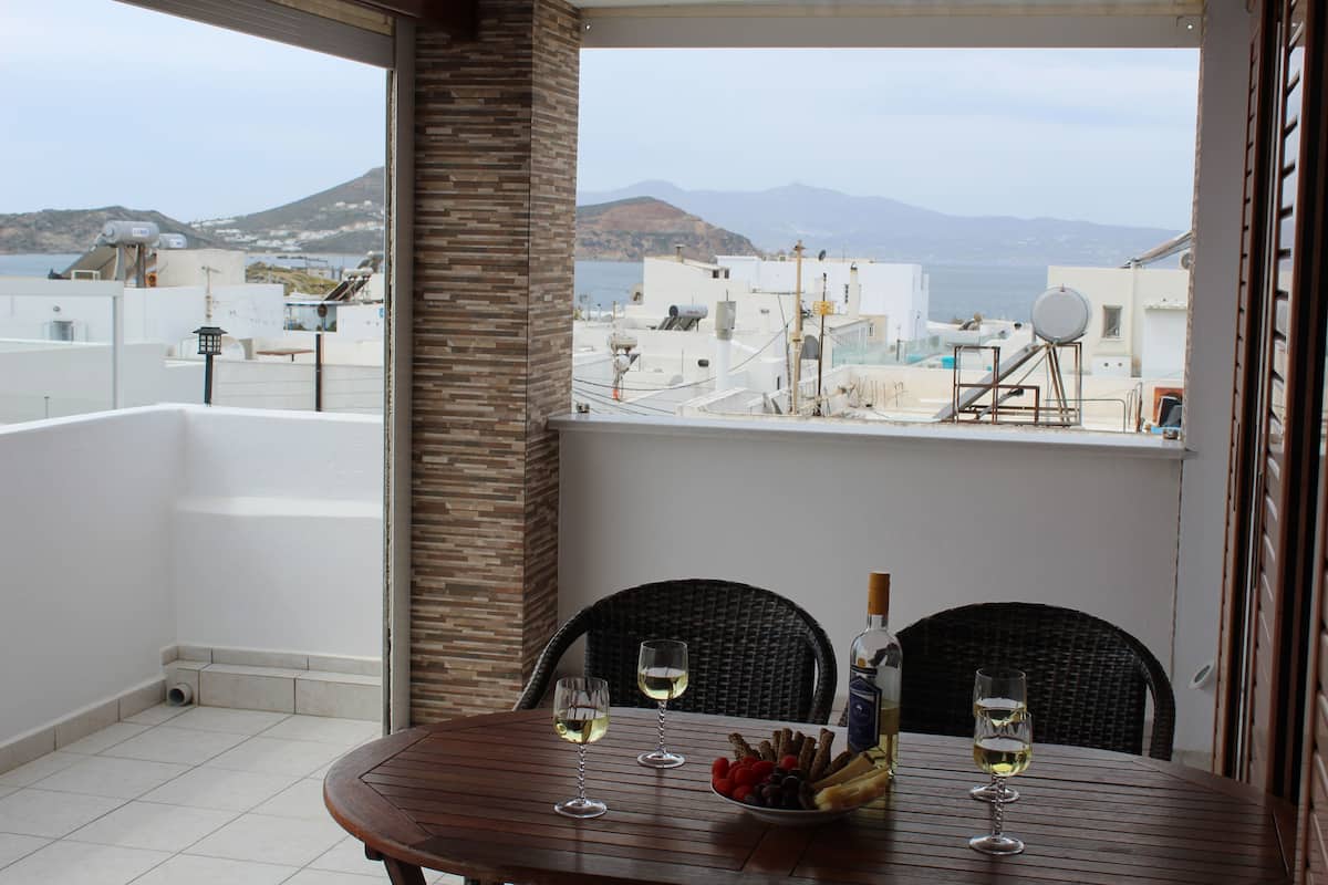 A balcony with a table set for two, two wine glasses, a bottle of wine, and a bowl of snacks.