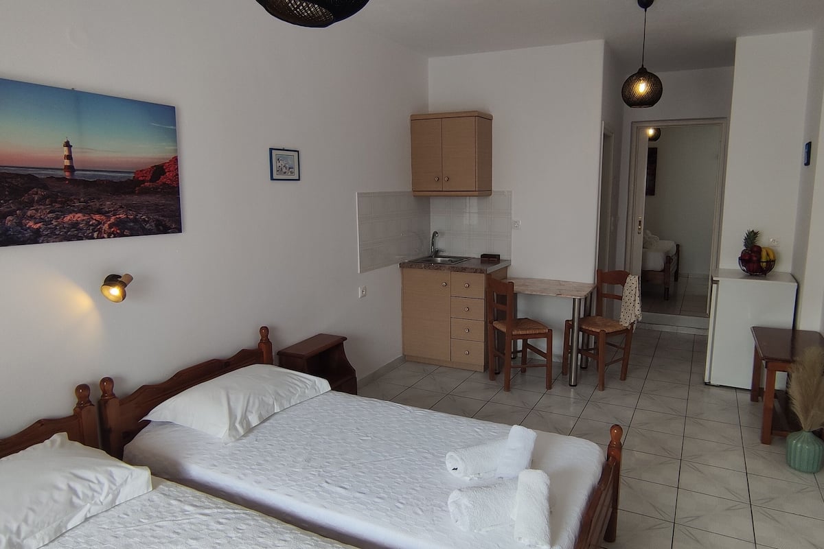 A bedroom with two beds, a small kitchenette, and a dining area.
