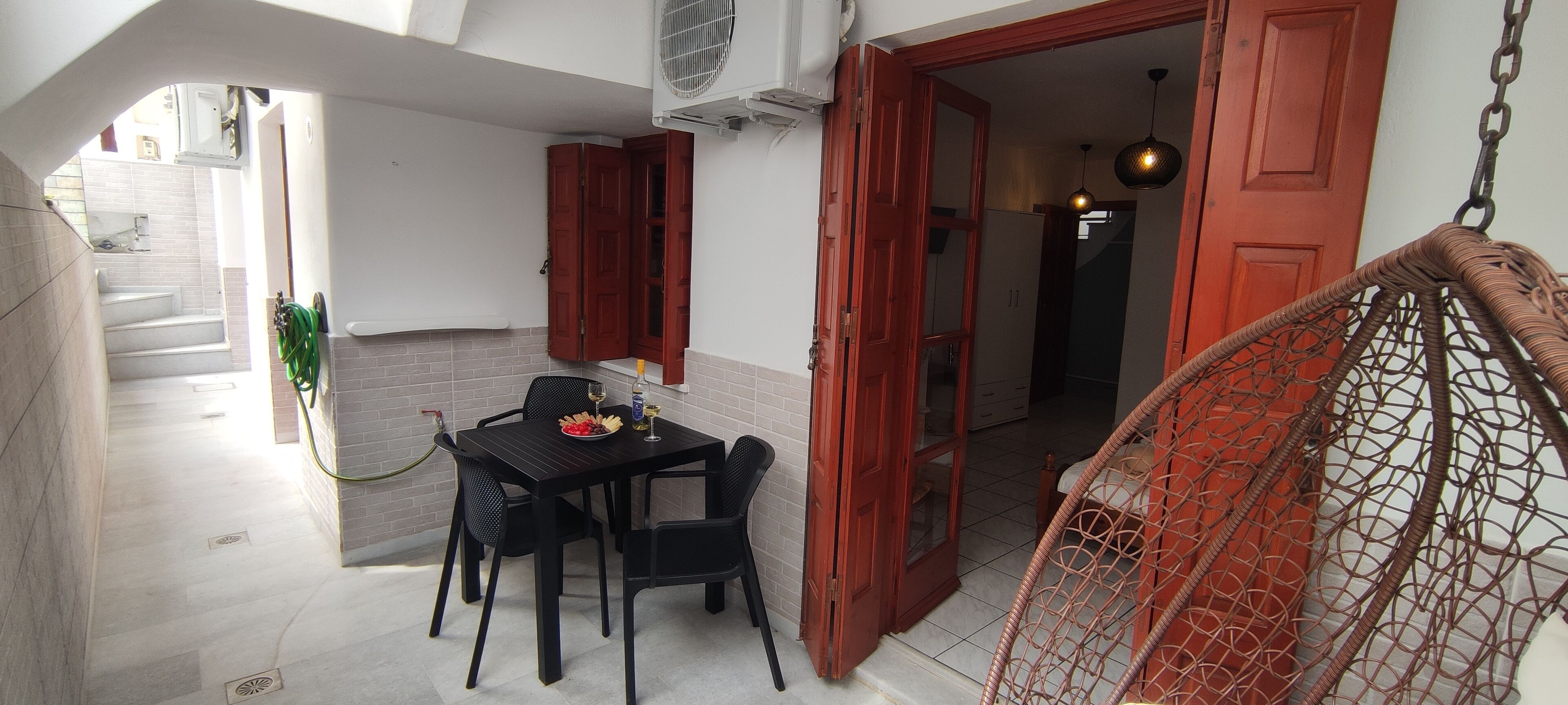 A small dining area with a table and chairs, a hanging chair, and a red door leading to another room.