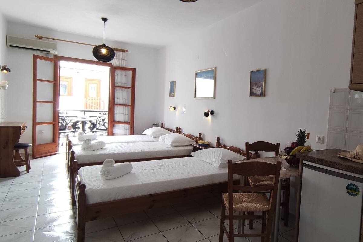 A room with two beds, a dining table, a kitchen area, and a small island with a sink.
