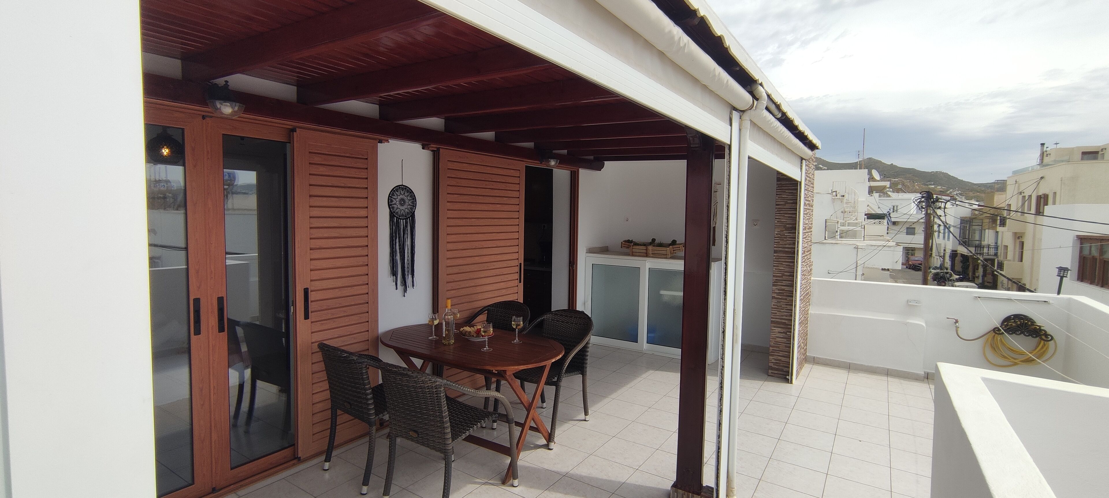 A covered outdoor dining area with a table and chairs, a dreamcatcher decoration, and a view of the surrounding buildings.