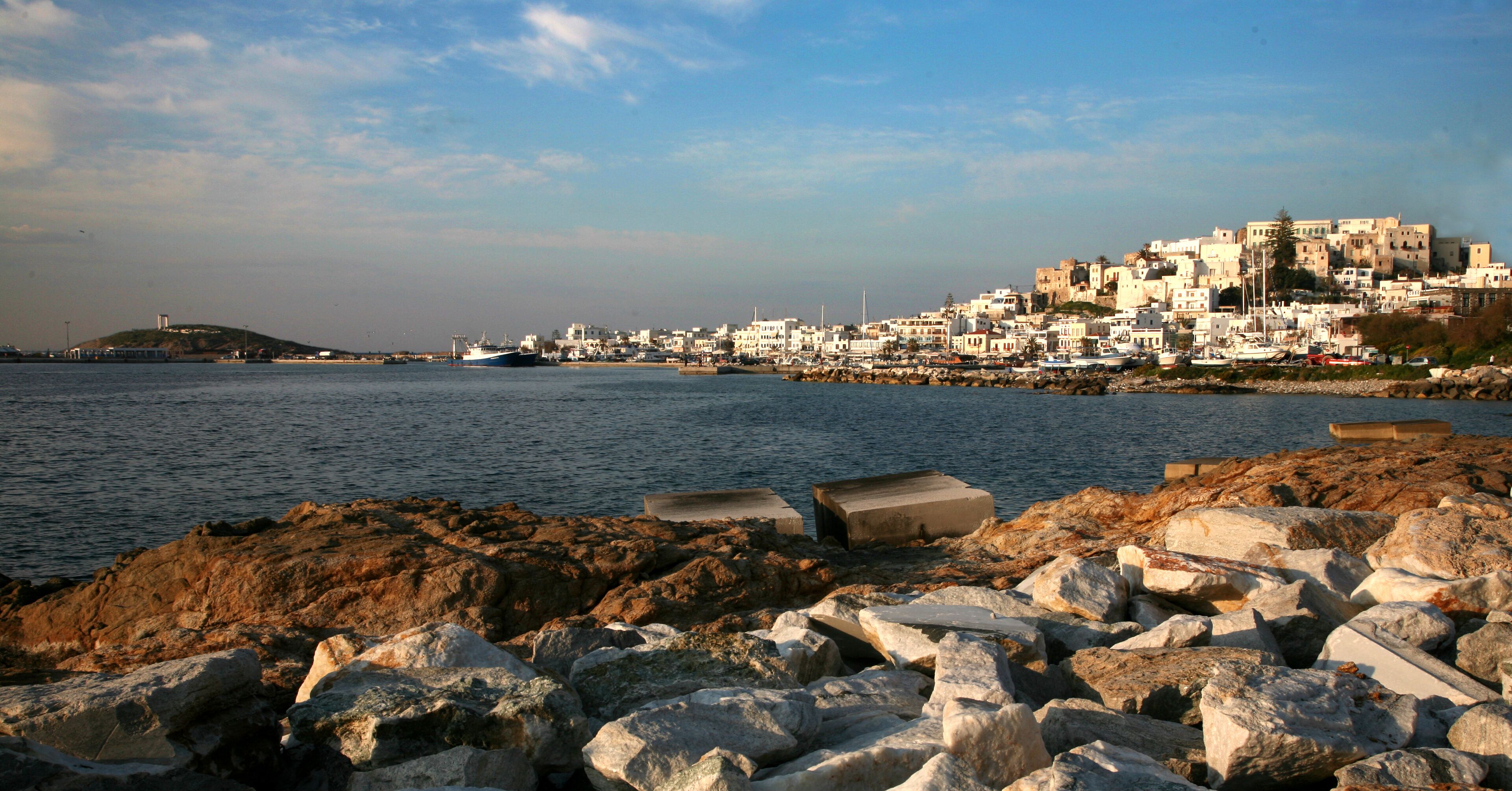 A coastal town with a rocky shoreline, a large body of water, and a densely packed cluster of buildings on a hill.