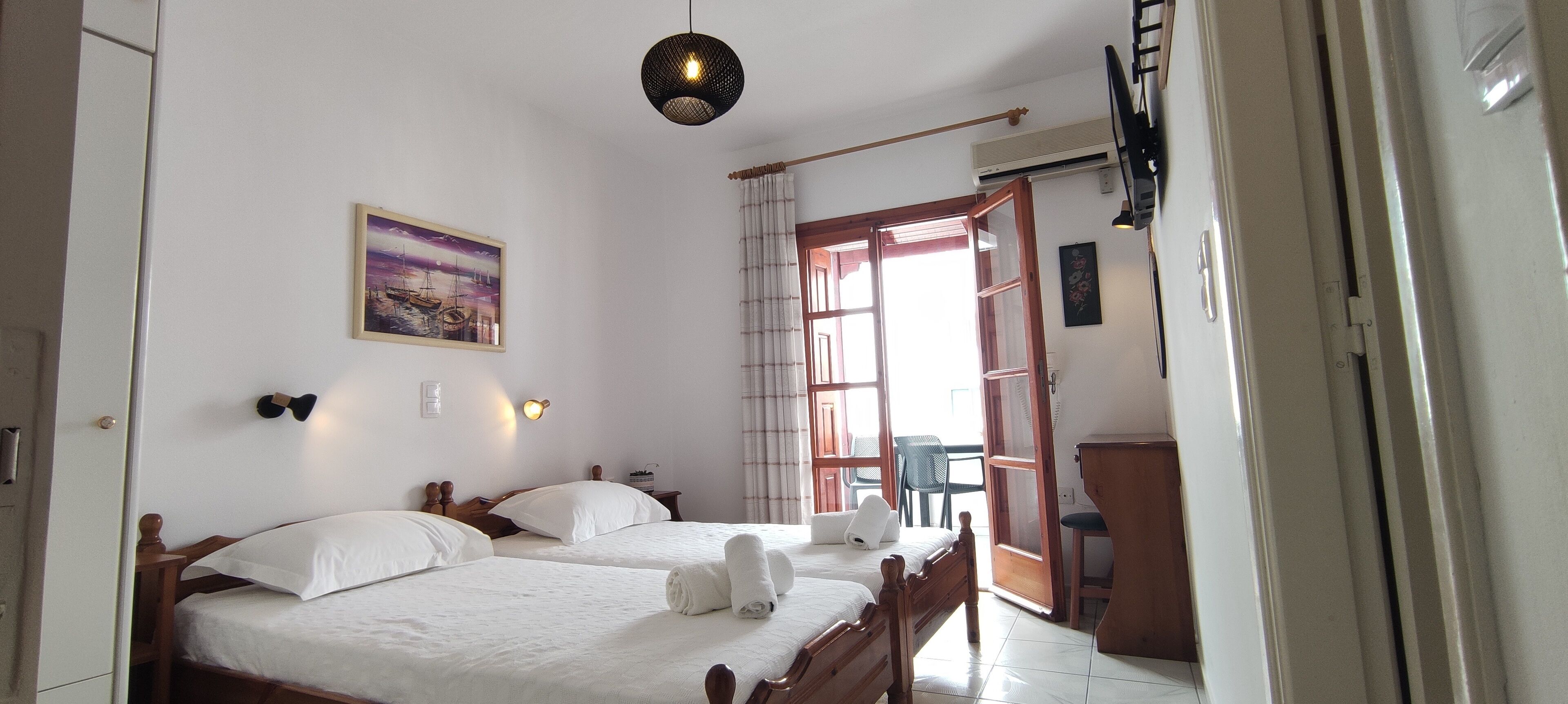Une chambre d’hôtel avec deux lits, un tableau au mur, un luminaire au plafond et une vue sur l’extérieur par une fenêtre.