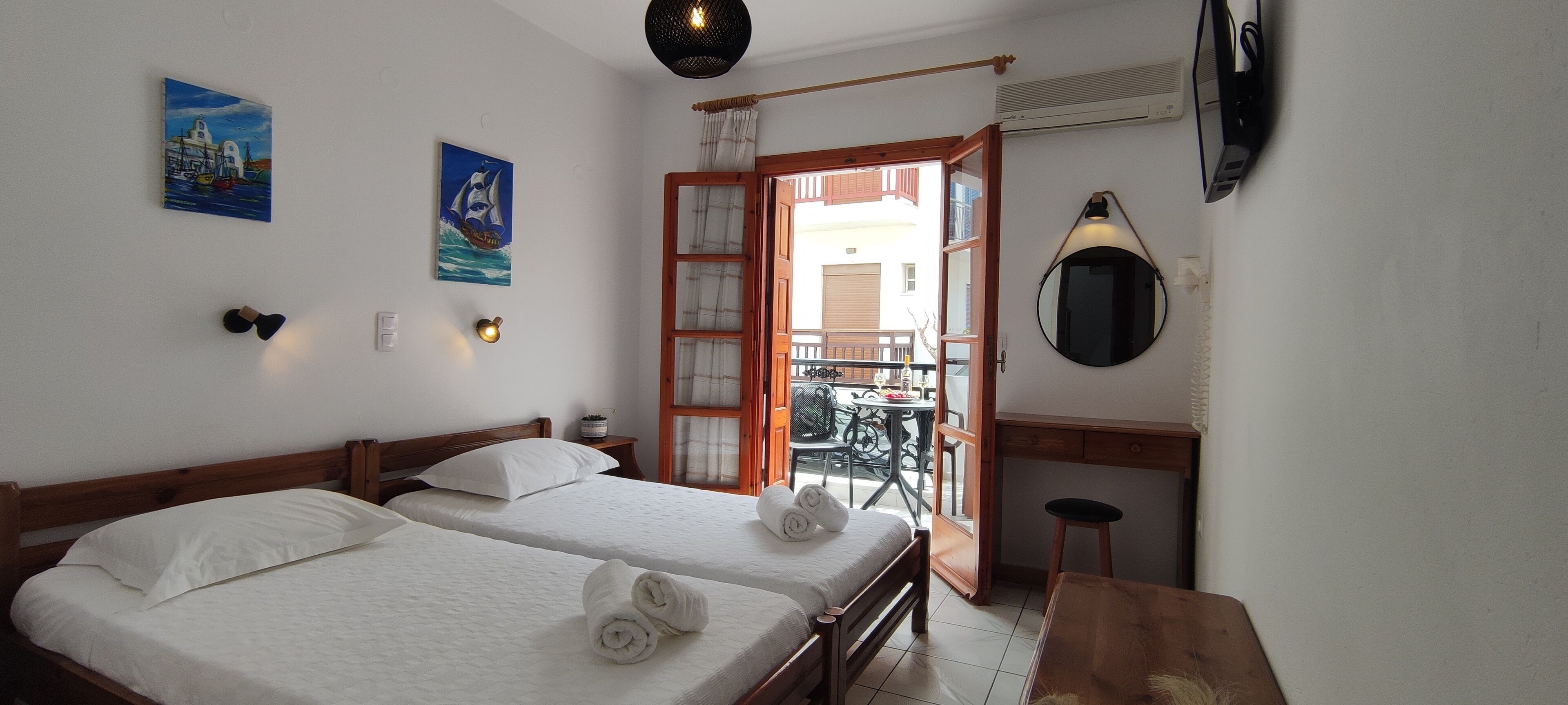 Ein Zimmer mit zwei Betten, einem Holztisch, einem Spiegel und einem Balkon mit Tisch und Stühlen.