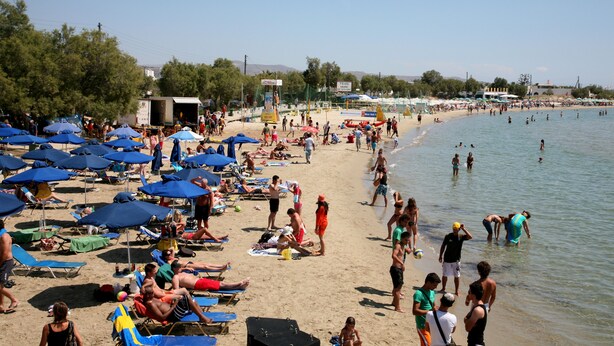 A crowded beach with numerous umbrellas and people enjoying the sand and water.