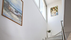 A staircase with a handrail, a painting of a beach scene, and a window.
