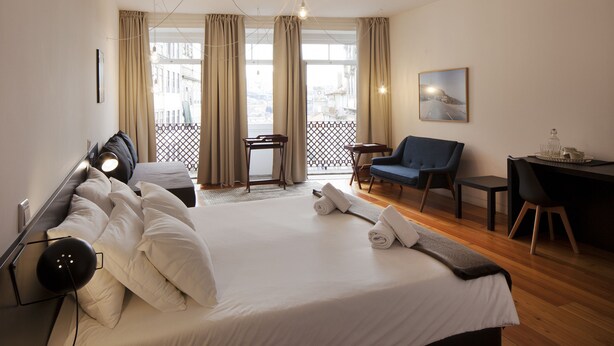 Ein Hotelzimmer mit einem großen Bett, einem Schreibtisch, einem Stuhl und einem Balkon mit Vorhängen.