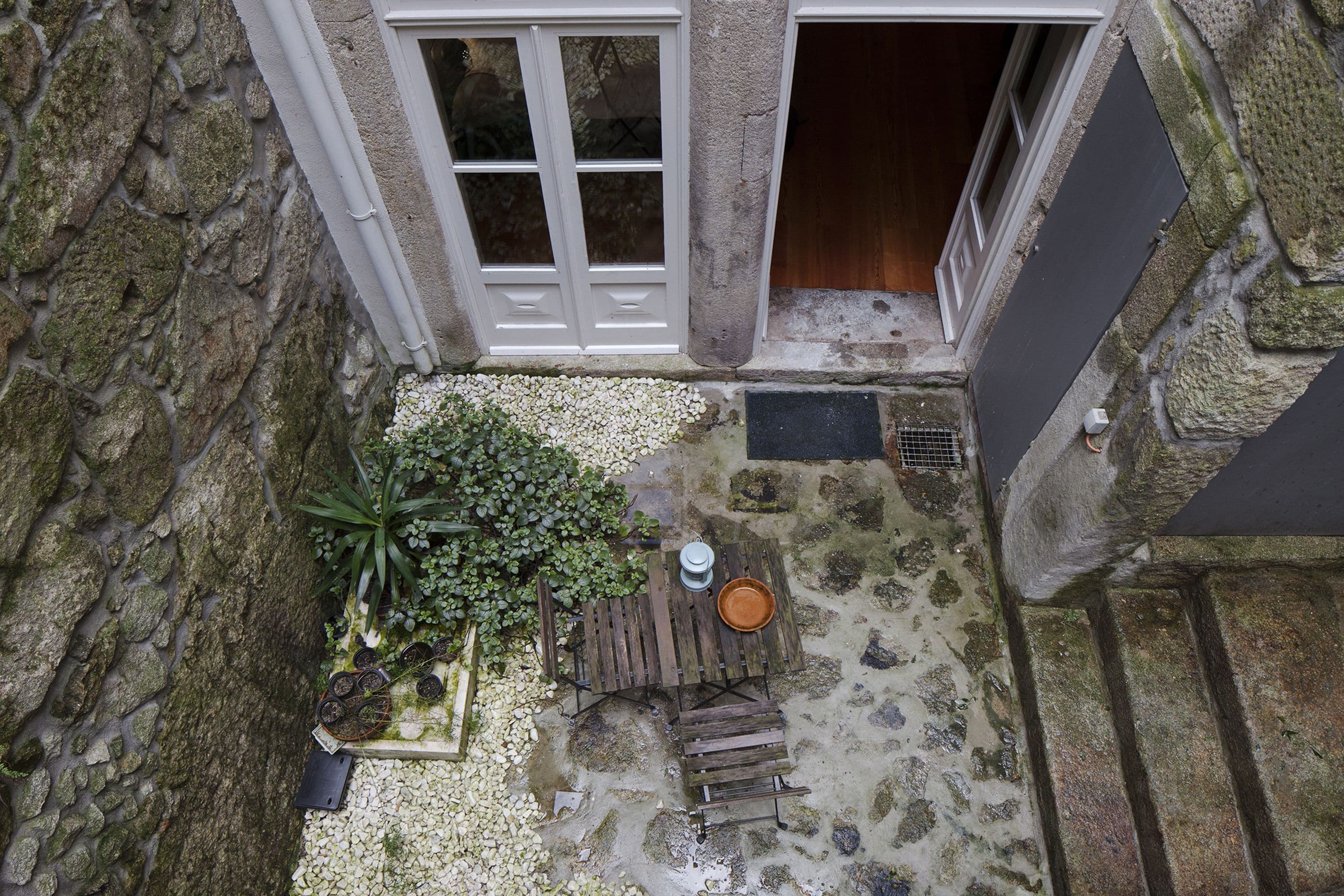 A stone building with a wooden deck, a white door, and a small garden area with plants and a table.