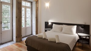 Ein Schlafzimmer mit einem großen Bett, zwei Nachttischen und Blick durch eine Tür auf einen Außenbereich.