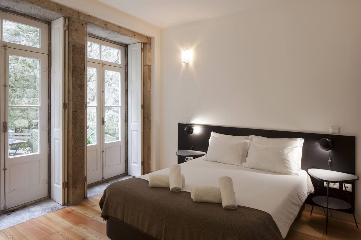 A bedroom with a large bed, two bedside tables, and a view through a door to an outdoor area.