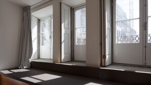 Ein Zimmer mit großen Fenstern, einer Sitzbank und Blick auf Gebäude.
