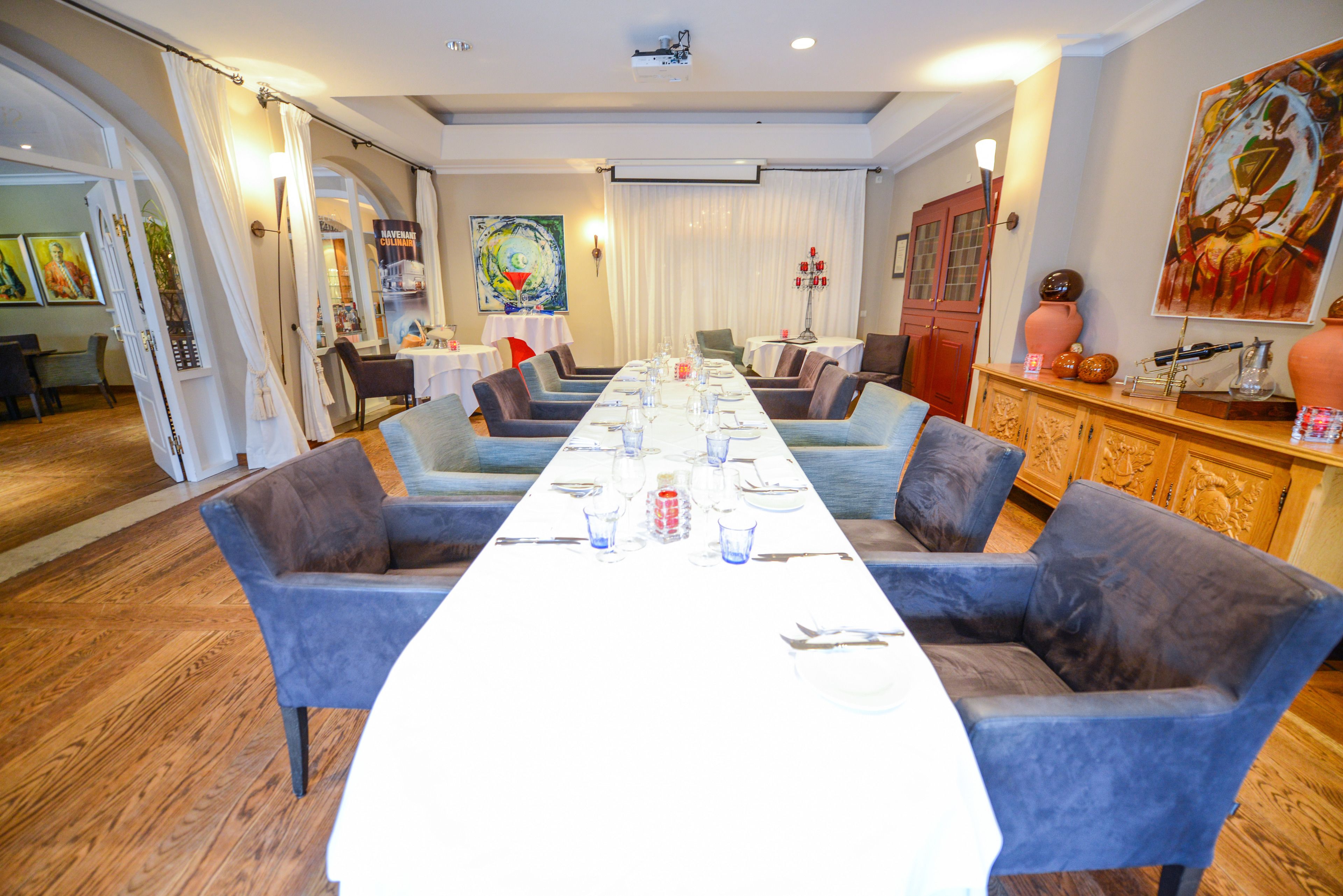 Ein Essbereich mit einem langen Tisch, gedeckt für eine Mahlzeit, umgeben von blau gepolsterten Stühlen.