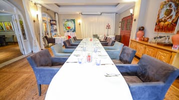 Ein Essbereich mit einem langen Tisch, gedeckt für eine Mahlzeit, umgeben von blau gepolsterten Stühlen.