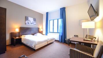 Een hotelkamer met een bed, een bureau, een stoel, een lamp en een raam met gordijnen.
