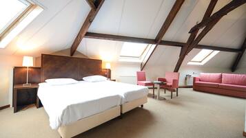 A bedroom with a large bed, a desk, a chair, and a sofa. There are skylights on the ceiling.
