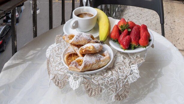 Un balcón con una mesa dispuesta para el desayuno, que incluye bollería, fresas y un plátano.
