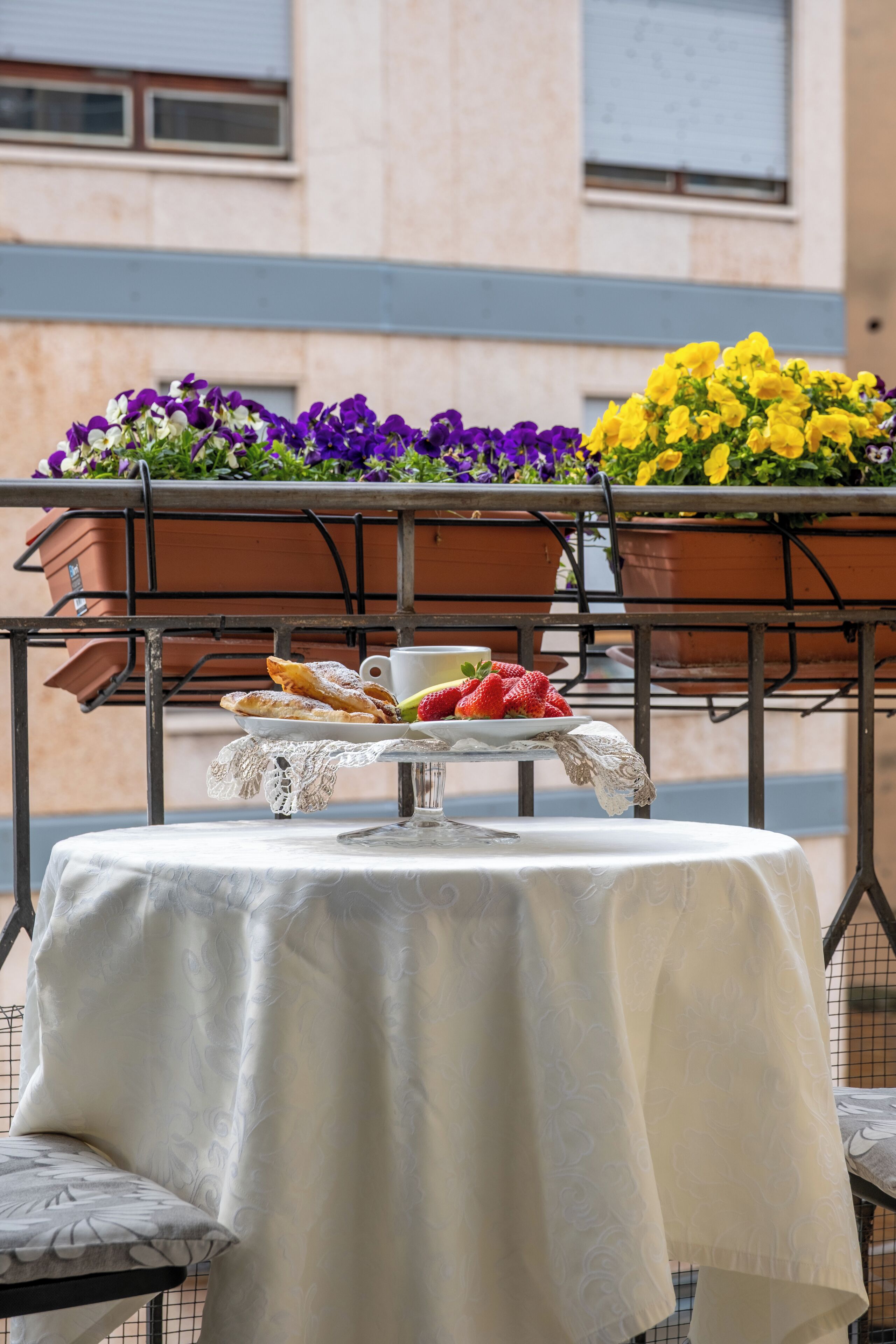 A table set with pastries, a cup, and a plate of strawberries, with flower pots in the background.