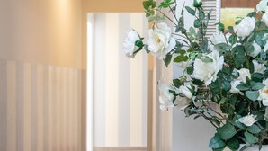 Un pasillo con una pared a rayas, un jarrón blanco con flores blancas y una alfombra roja estampada.