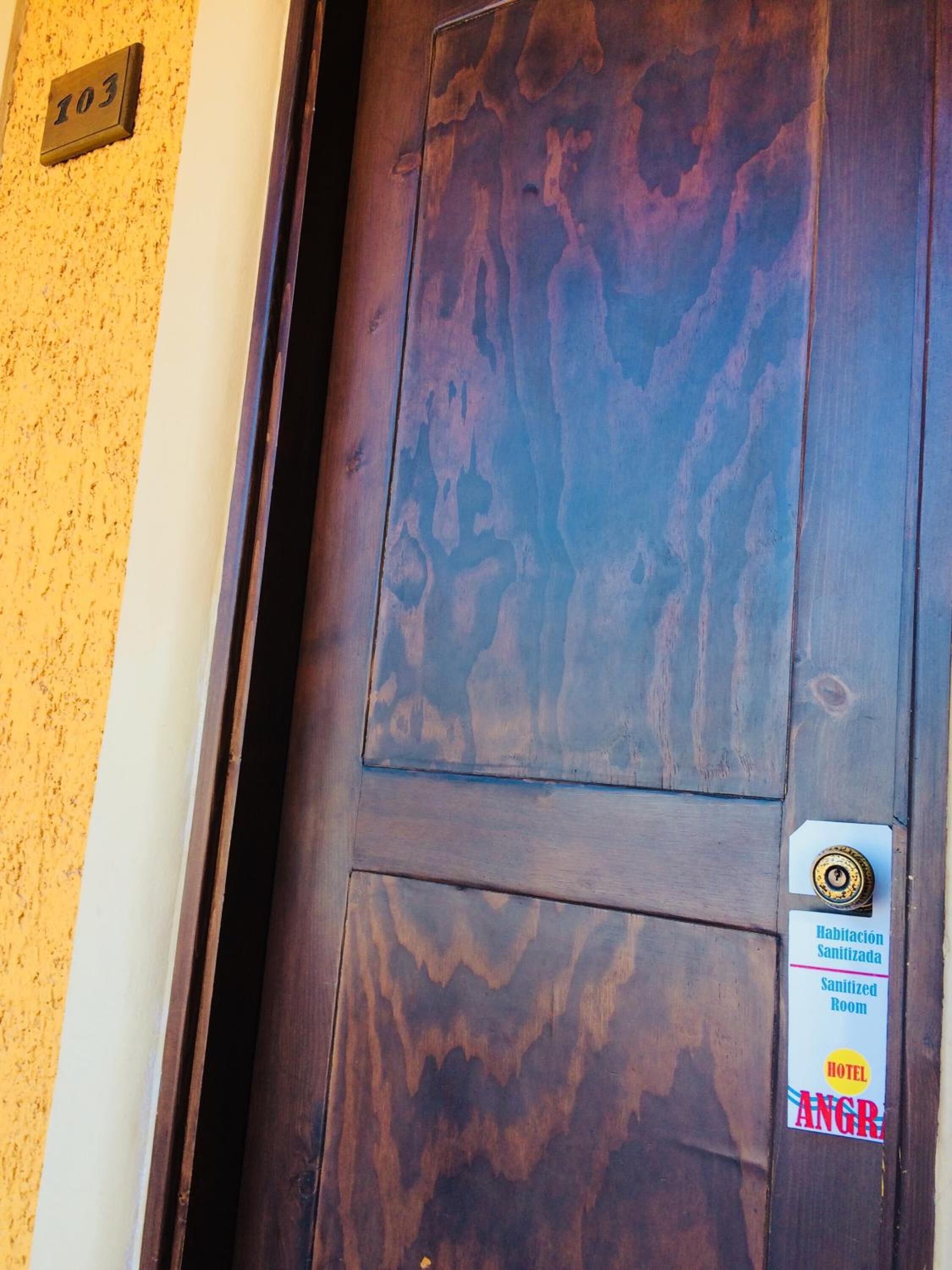 Une porte de chambre d’hôtel avec une plaque indiquant le numéro de la chambre, un panneau signalant qu’il s’agit d’une chambre désinfectée, et le nom de l’hôtel.