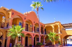 Un edificio de varios pisos con fachada amarilla, balcones arqueados y palmeras.