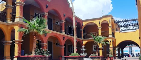A courtyard with a red and yellow building, palm trees, and two white poodles.