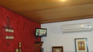 Une pièce avec un mur rouge, un téléviseur fixé au mur, un appareil de climatisation et des tableaux encadrés.