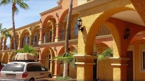 Un hôtel avec une rangée d’arcades, des palmiers et une voiture garée.