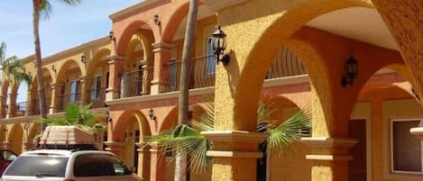 A hotel with a row of arches, palm trees, and a parked car.