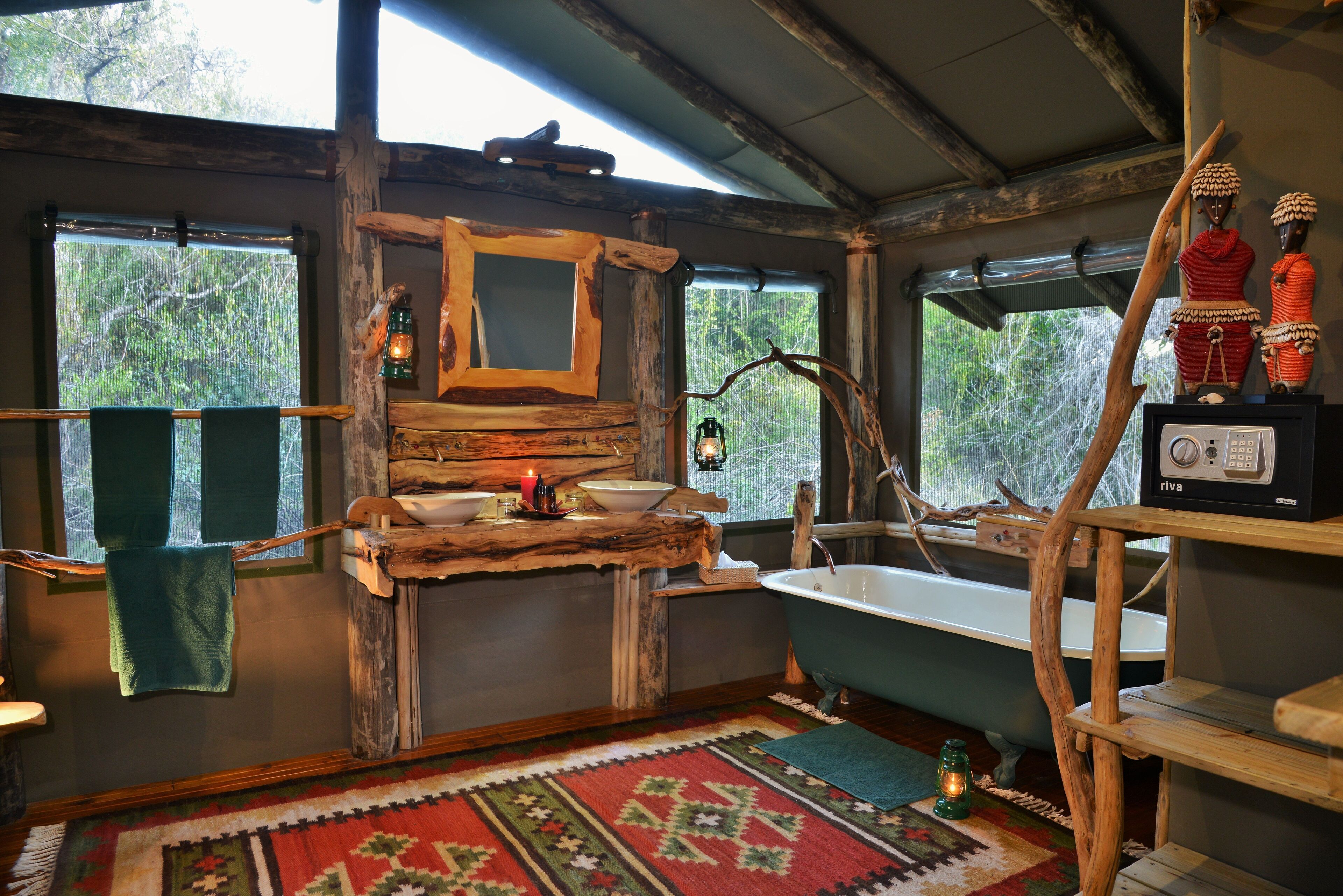 A rustic bathroom with a wooden vanity, a freestanding bathtub, and a large window with a view of trees.