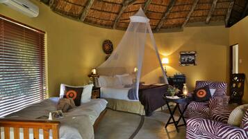 A room with a bed, a daybed, a small table with a lamp, a zebra-patterned sofa, and a mosquito net over the bed.