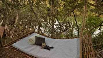 A hammock with a blanket and pillows, surrounded by trees.