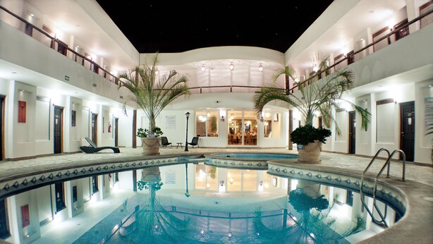 A hotel pool area with a central pool, palm trees, and a covered seating area. - Hotel  Maioris La Paz (La Paz)