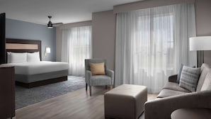 A modern hotel room with a bed, a grey armchair, a sofa, and a small table. - Homewood Suites by Hilton Orlando Airport (Orlando)