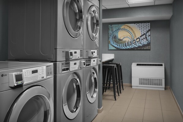 A laundry room with stacked washers and dryers, a digital control panel, and a wall-mounted air conditioner.