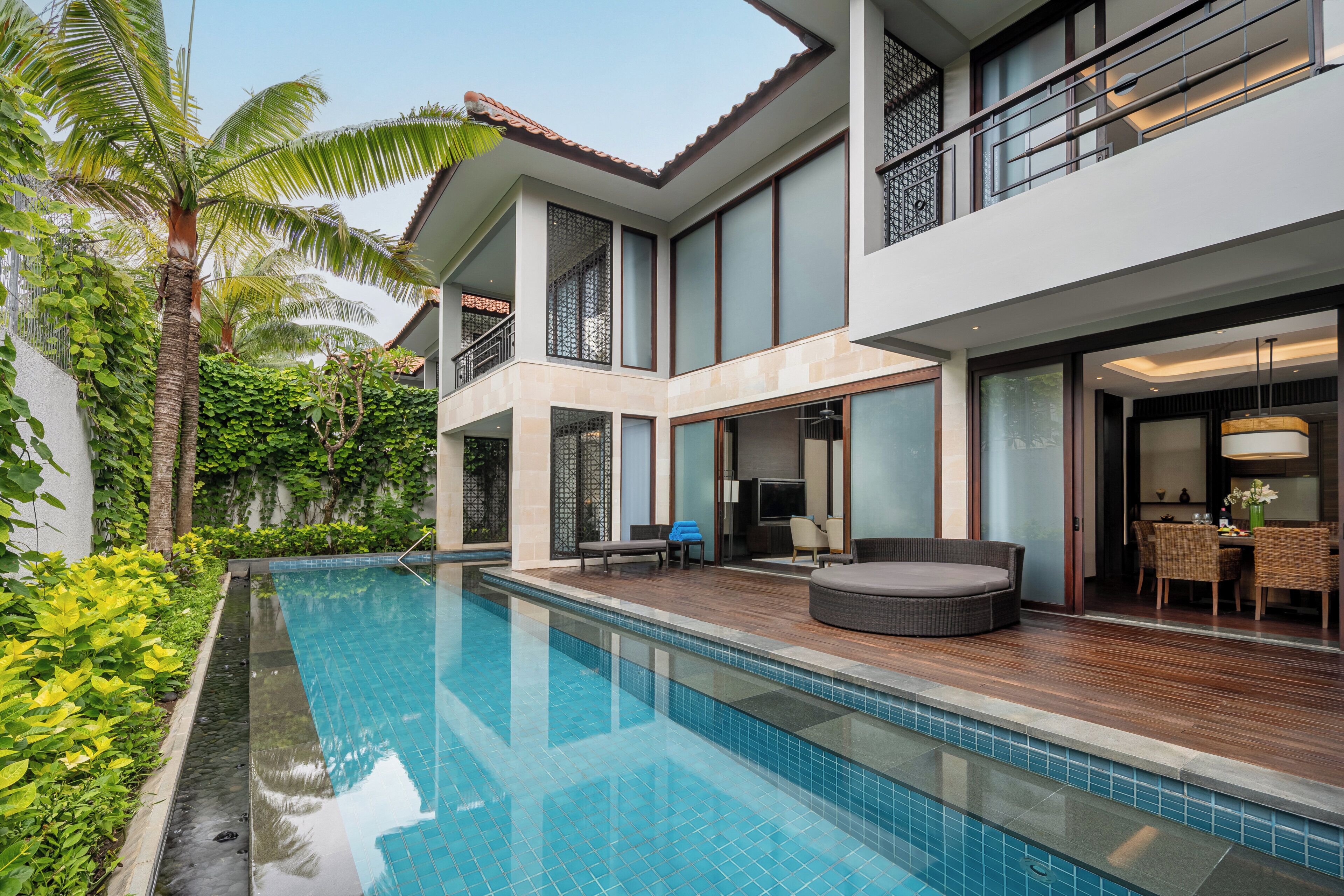 A modern two-story house with a swimming pool, outdoor seating, and lush greenery.
