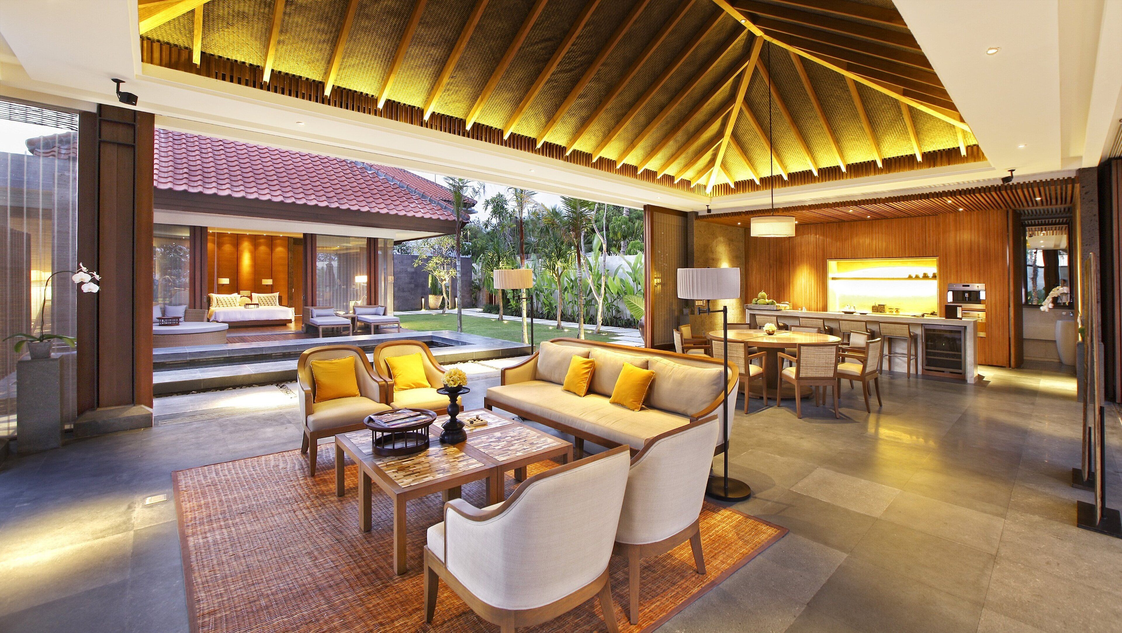 A spacious living area with a sofa, chairs, and a coffee table. A kitchen with a bar and a dining area are visible in the background.