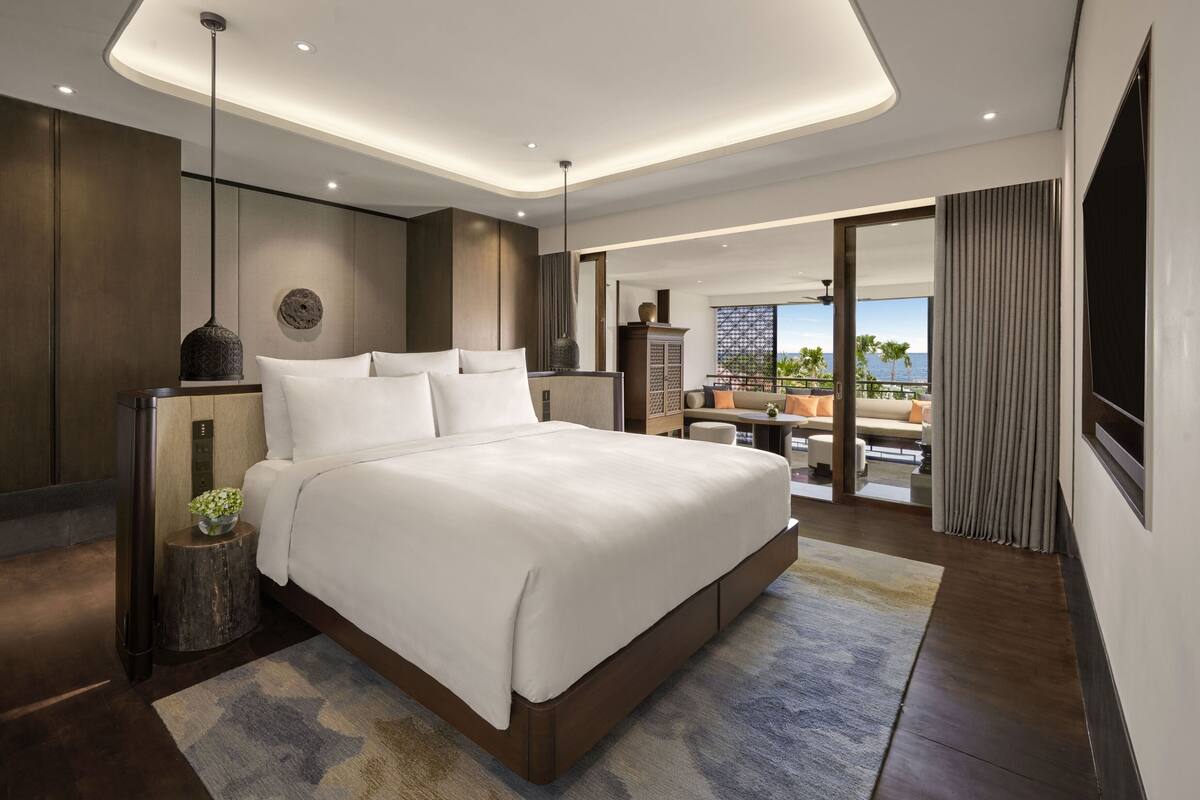 Une chambre d’hôtel moderne dotée d’un grand lit, offrant une vue sur l’océan et disposant d’un balcon avec des sièges extérieurs.