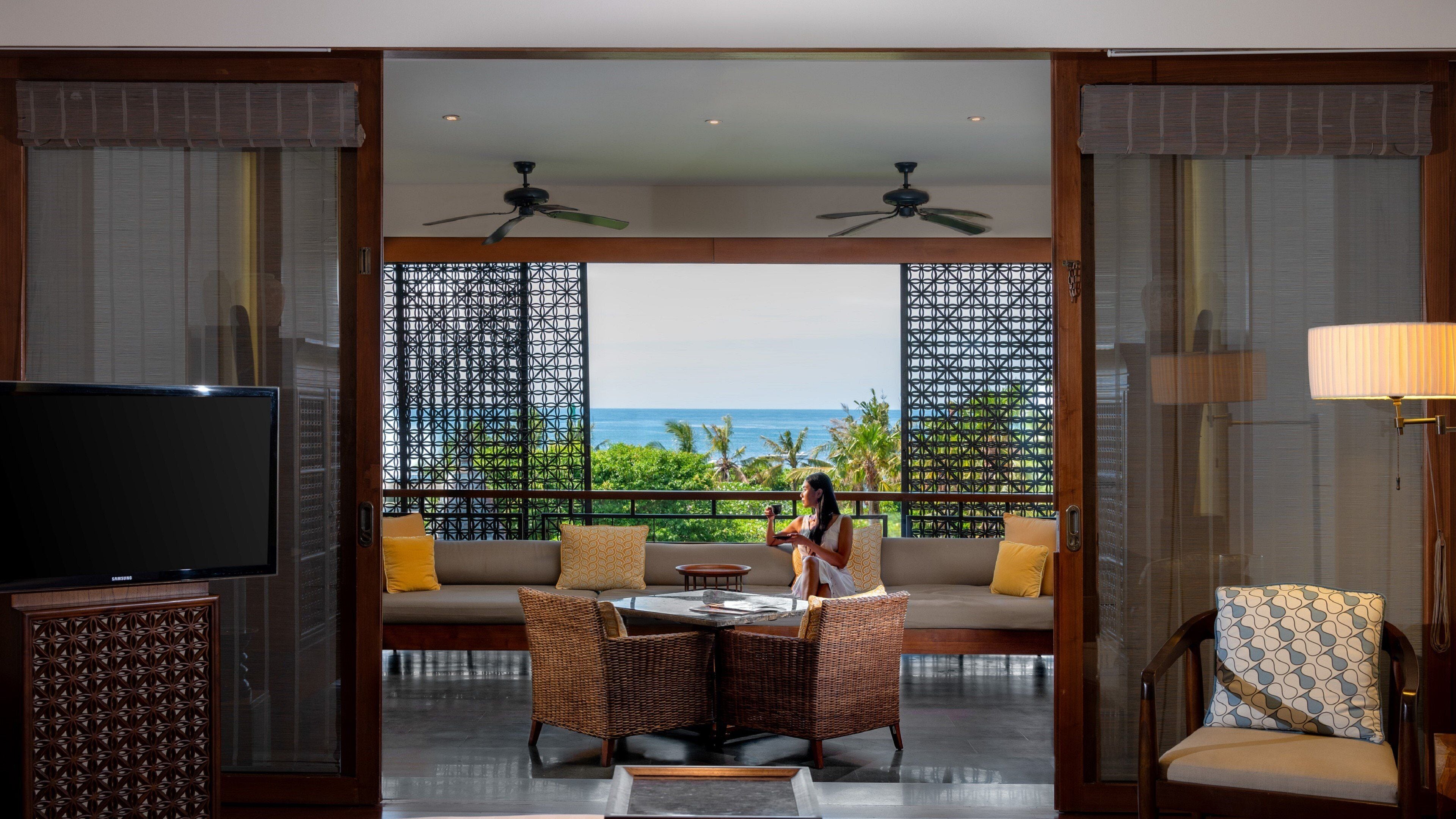 A room with a television, a table with chairs, a sofa, and a view of the ocean.