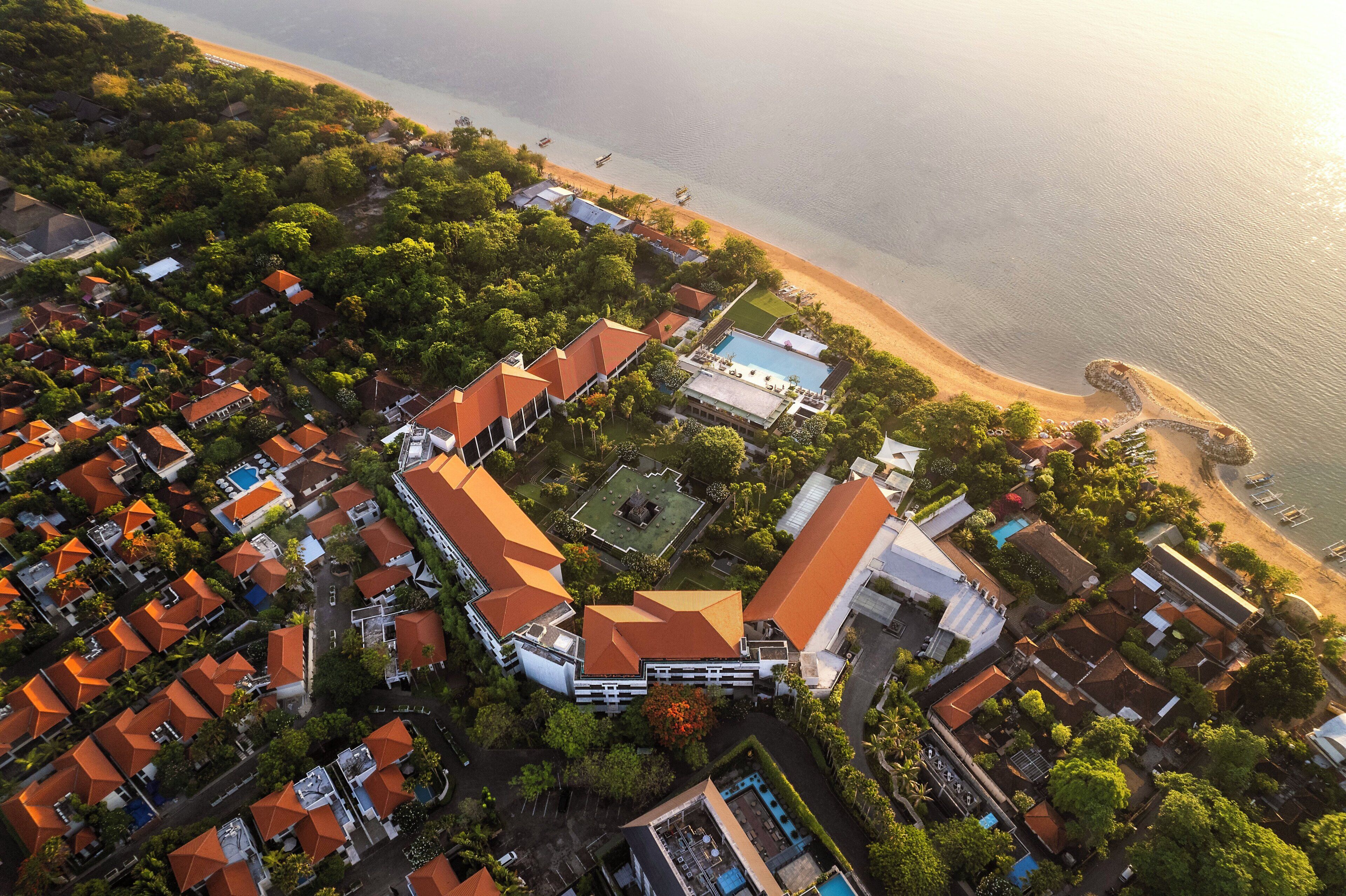 An aerial view of a coastal resort with multiple buildings, a swimming pool, and a beach.