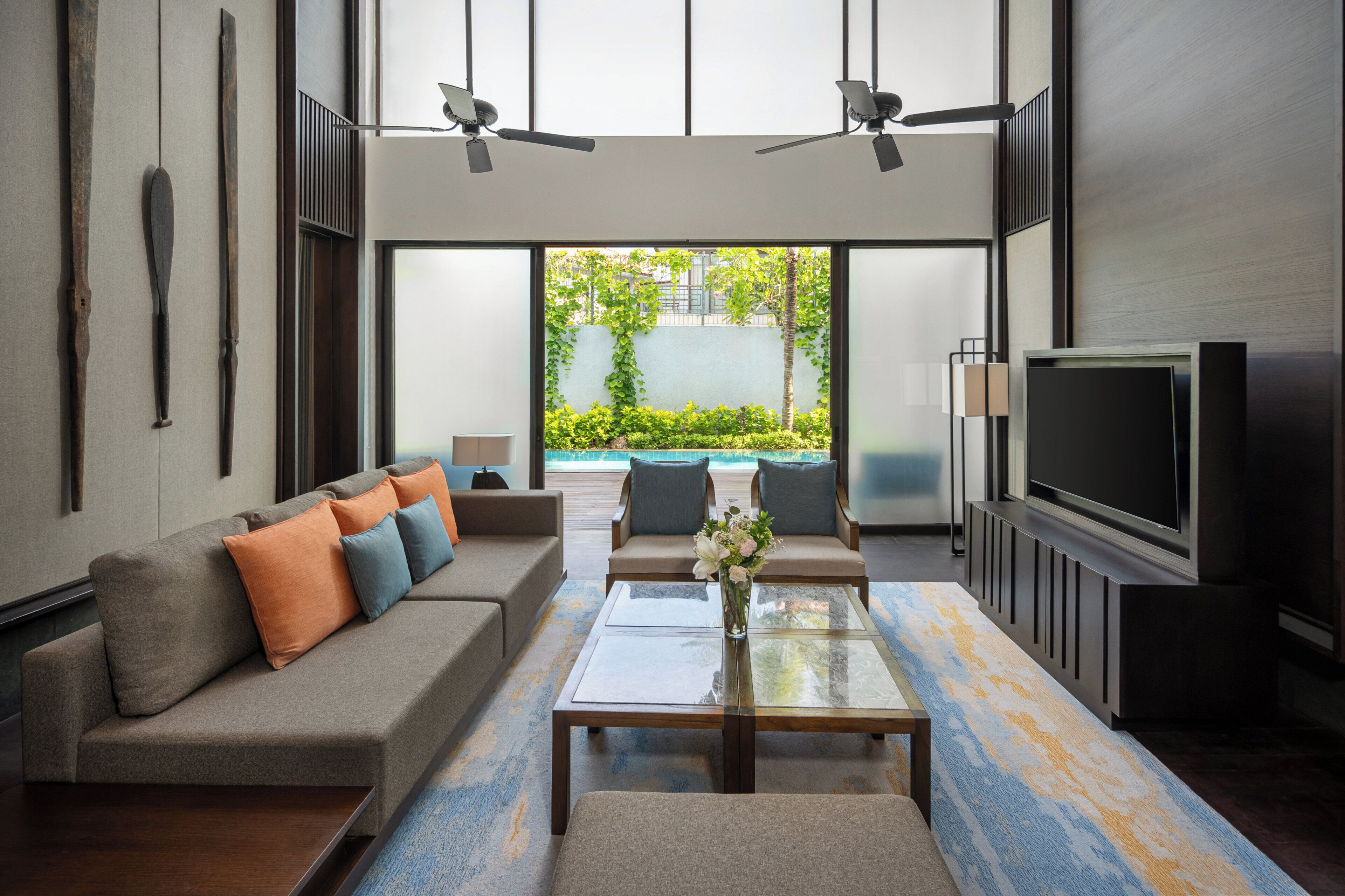 A modern living room with a sofa, coffee table, TV, and ceiling fans.
