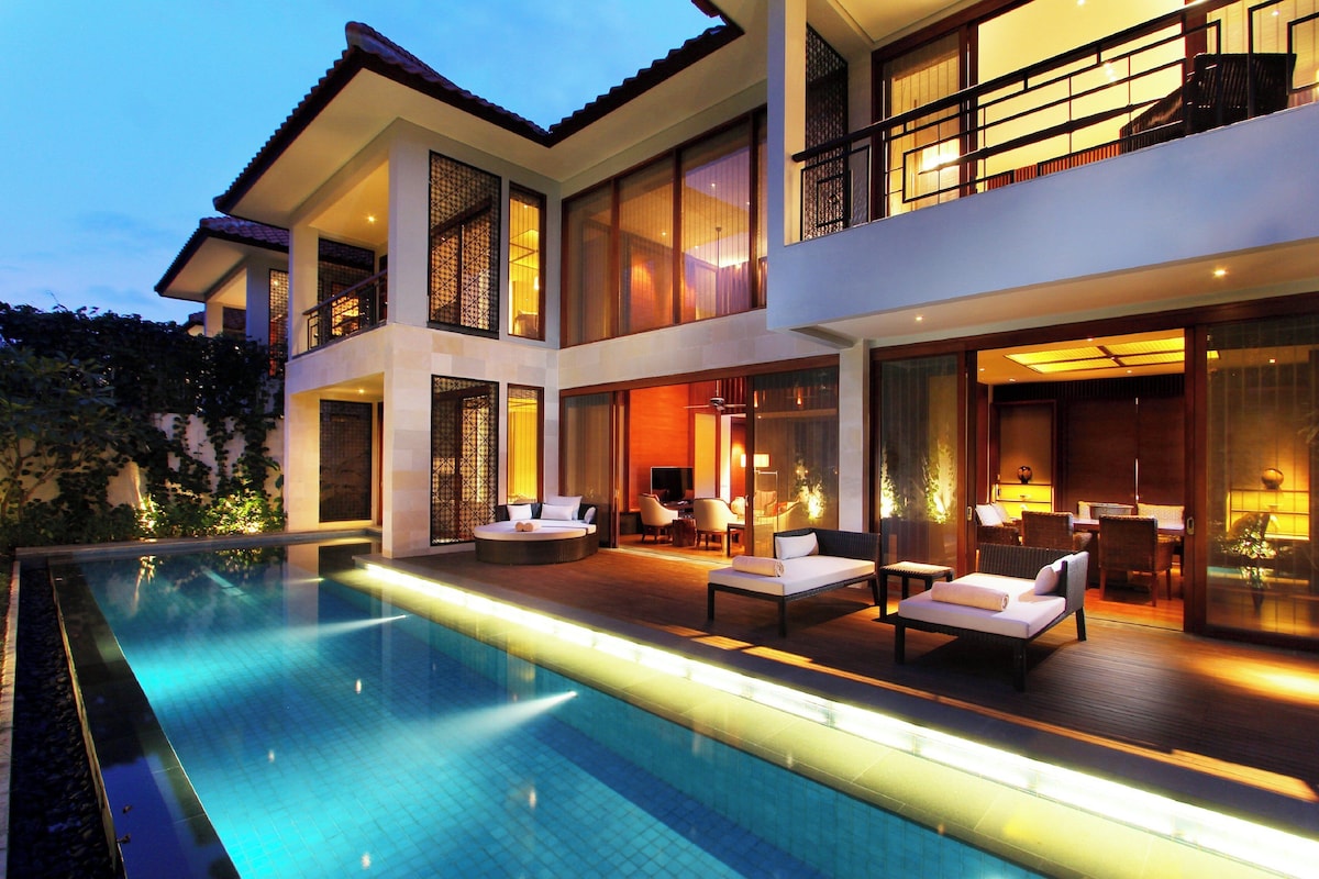 A modern two-story house with a swimming pool, outdoor seating, and large windows.