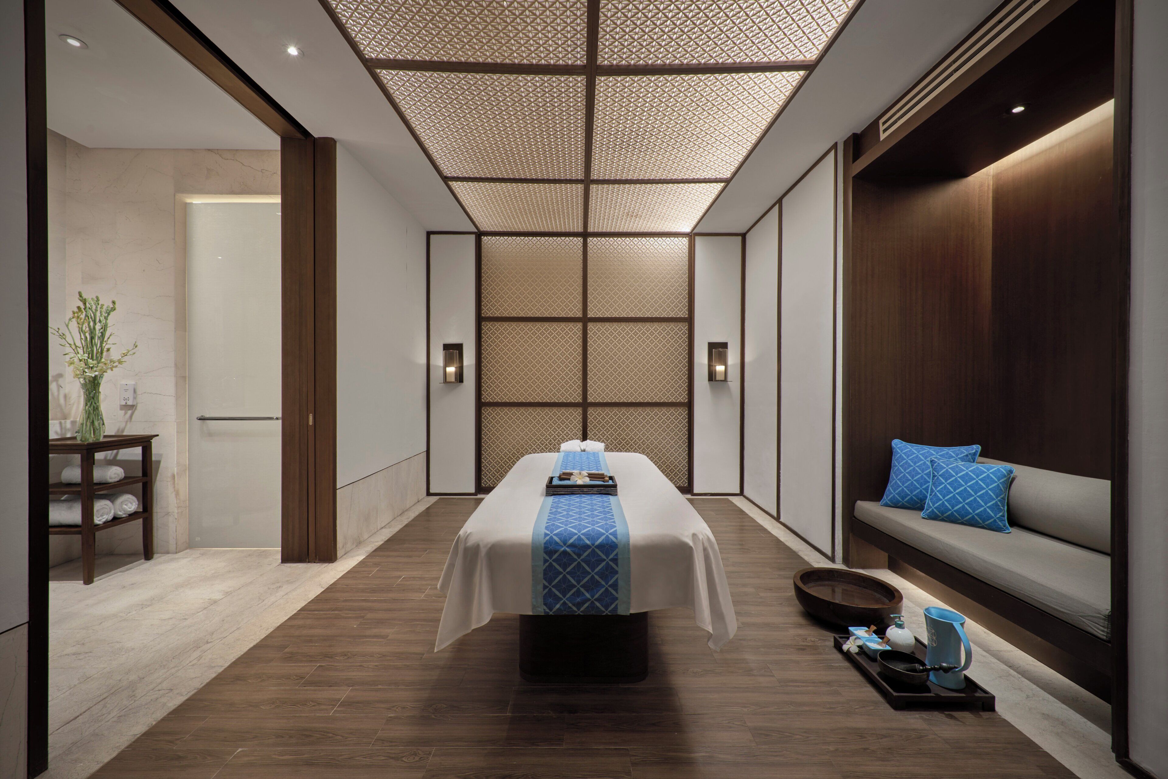 Een moderne spa ruimte met een massagetafel, een zithoek met kussens, en een houten vloer.