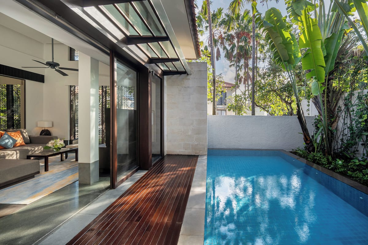 Un espace piscine intérieur moderne, doté d’une terrasse en bois, de portes vitrées et offrant une vue sur une végétation luxuriante.
