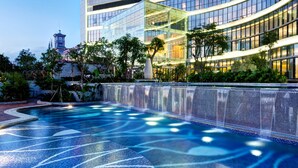 A modern hotel with a swimming pool, lush greenery, and a distinctive clock tower in the background. - Four Points by Sheraton Hainan, Sanya (Sanya)