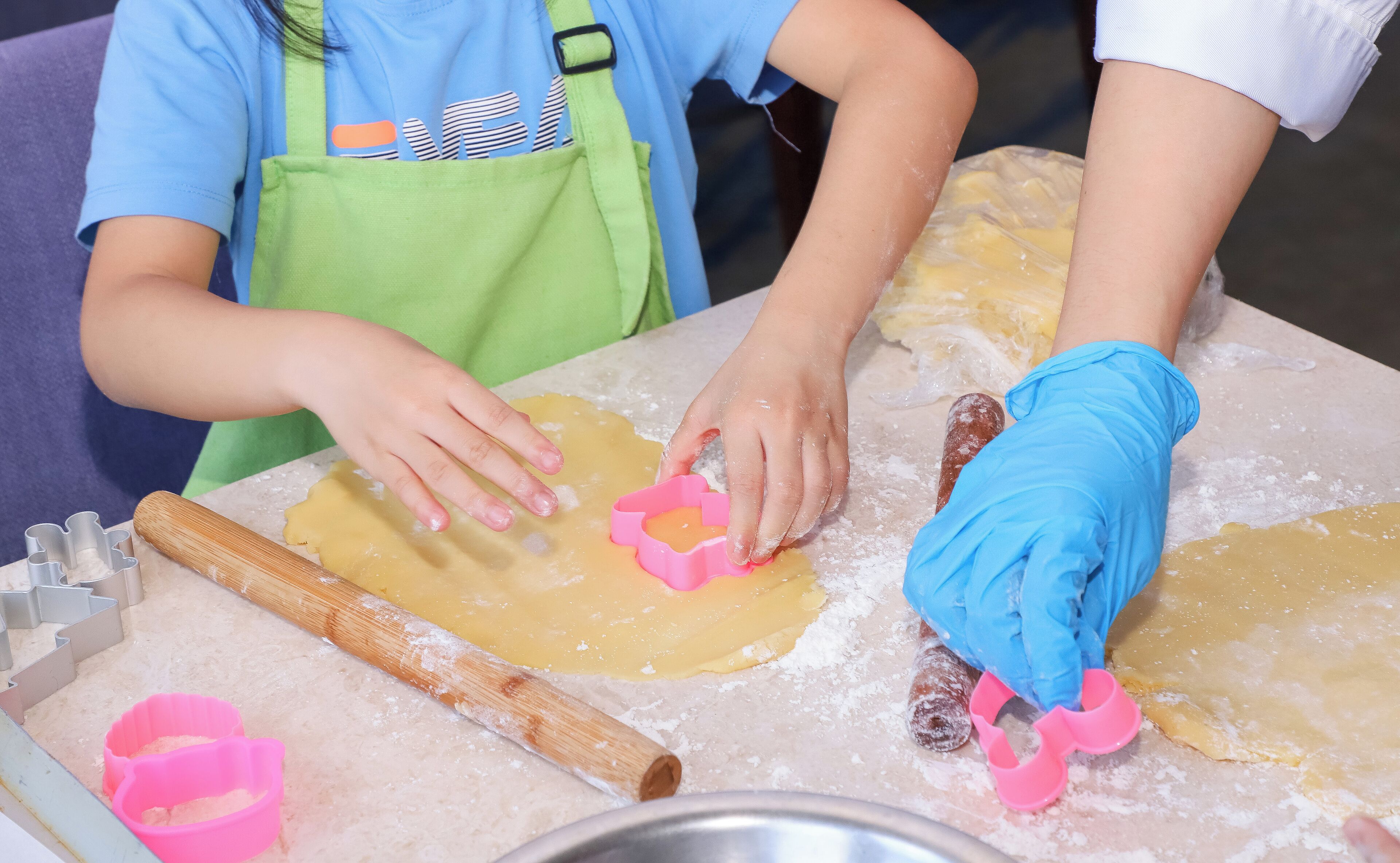 A person using a pink cookie cutter on dough on a floured surface.