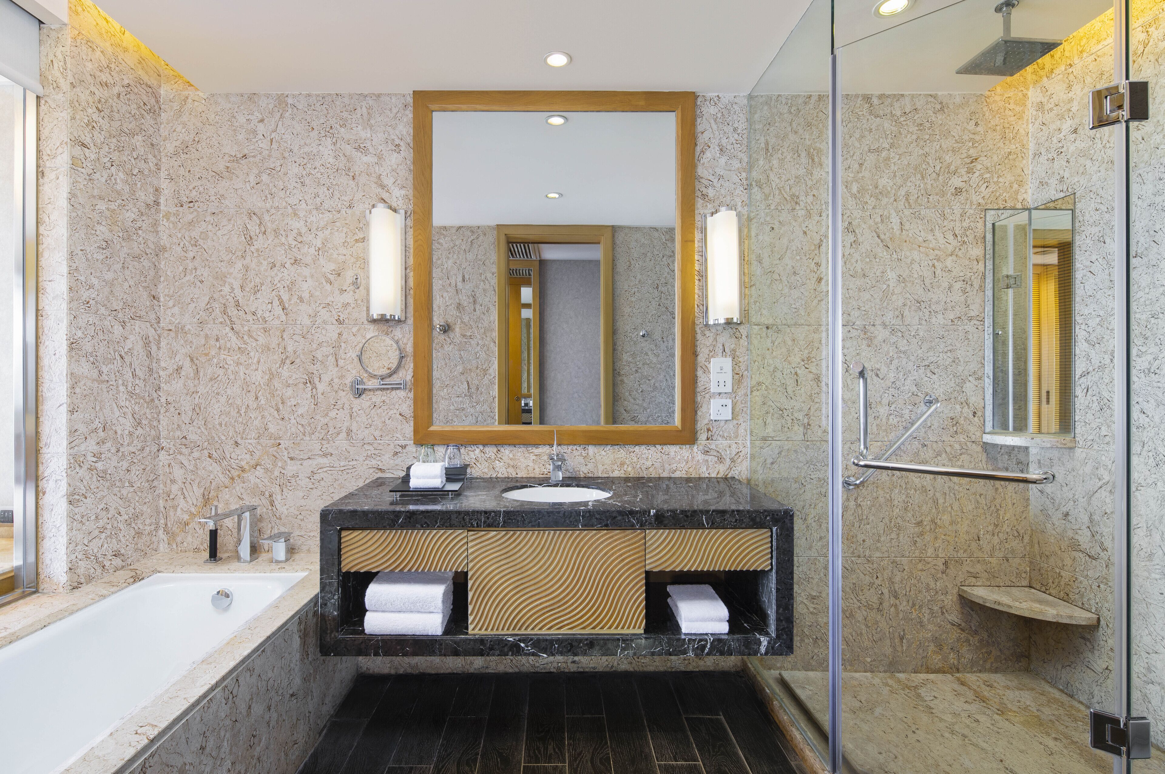 A modern bathroom with a marble sink, a large mirror, and a glass-enclosed shower.