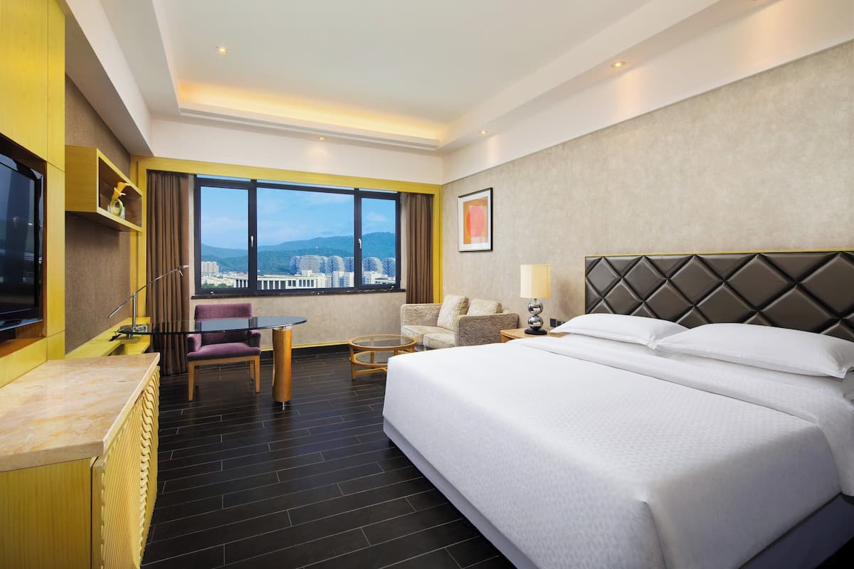 A hotel room with a large bed, a desk, a chair, and a TV.
