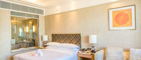 A hotel room with a large bed, two bedside tables, a glass coffee table, a sofa, and a large mirror.