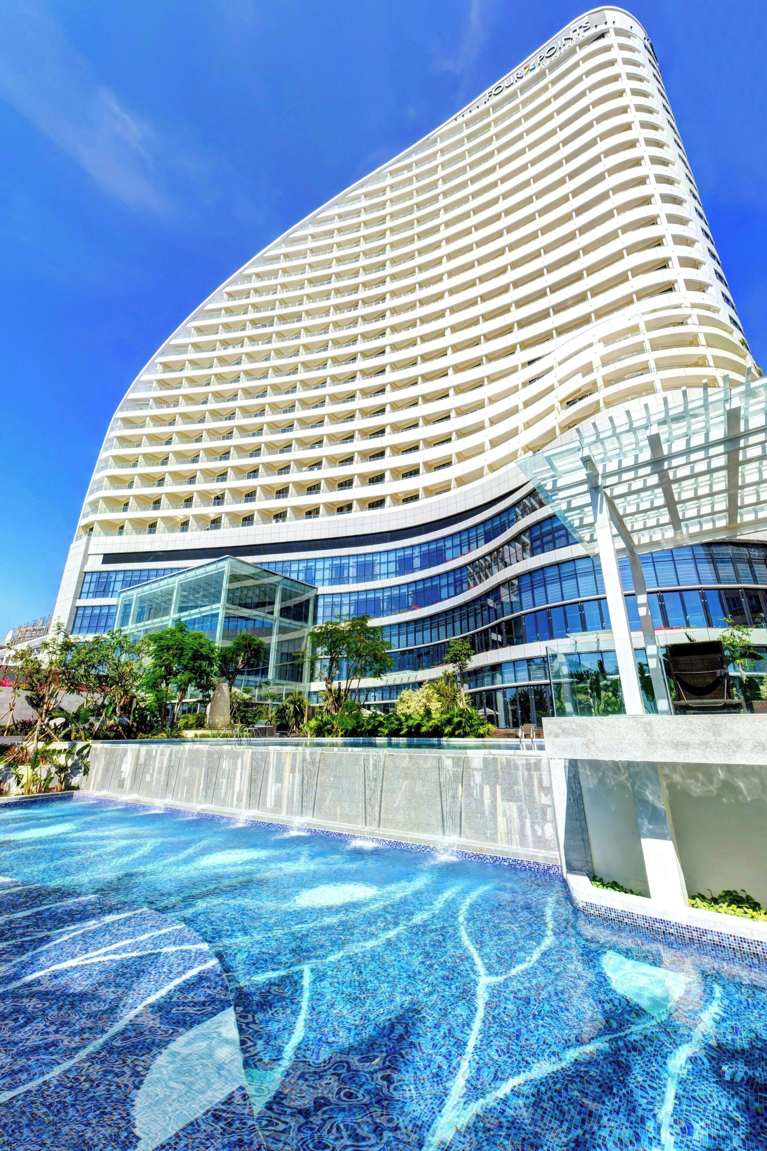 A modern hotel with a curved facade, large glass windows, and a pool area with a blue mosaic design.