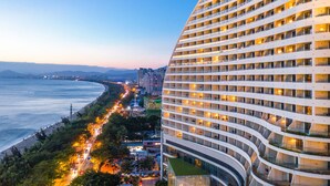 A high-rise hotel with multiple balconies, a curved facade, and a view of a beach and cityscape. - Four Points by Sheraton Hainan, Sanya (Sanya)